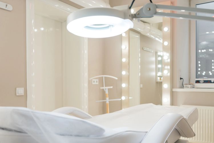 Clean and bright beauty treatment room with a white reclining chair and circular overhead light.