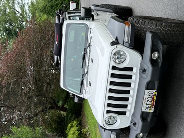 White Jeep Wrangler with roof rack in a suburban driveway.