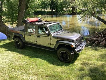 Jeep Gladiator parked by a riverside with trees.