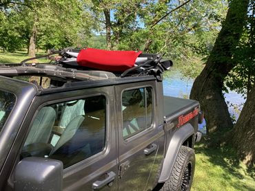 A black Jeep with a folded soft top parked near a lake surrounded by trees.