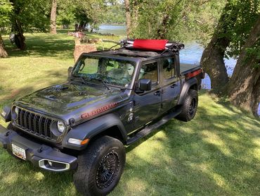 Black Jeep Gladiator parked by a scenic lakeside with trees and grass.
