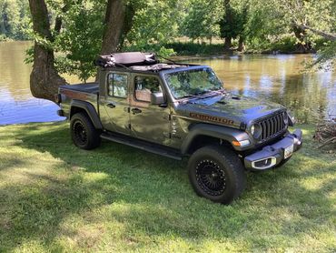 Jeep Gladiator parked by a lake surrounded by trees and greenery.