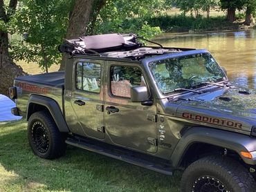 Black Jeep Gladiator parked by a river with open soft top.