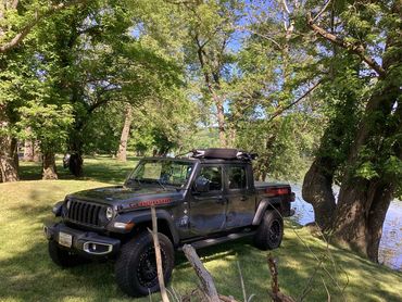 Black Jeep Gladiator parked by a lakeside with lush green trees.