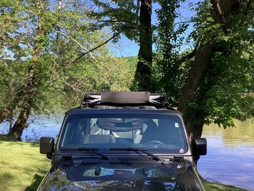 Black Jeep parked by a lake surrounded by trees on a sunny day.