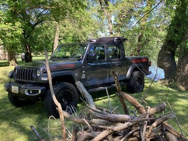 Black Jeep Gladiator parked near a lake surrounded by trees and sticks.