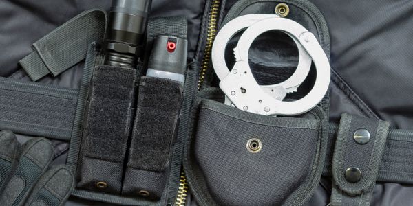Law enforcement gear including handcuffs, pepper spray, and flashlight on a tactical vest.
