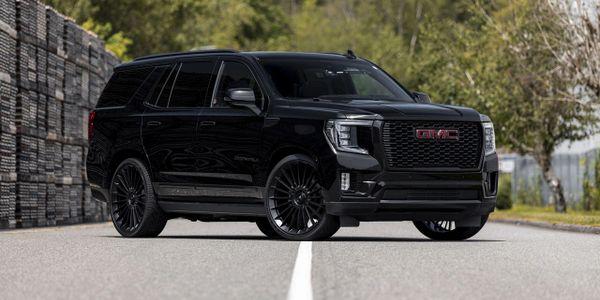 Sleek black GMC SUV parked on a road with greenery in the background.