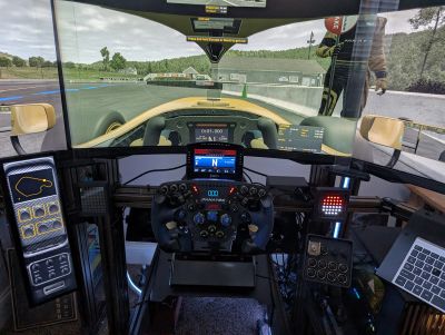 Sim racing setup with three screens and racing wheel.