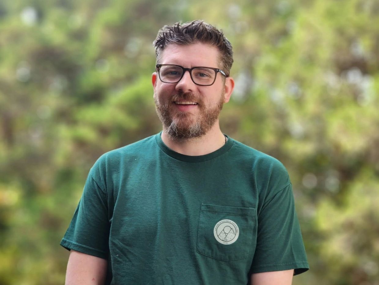 Smiling man with glasses in a green shirt outdoors.