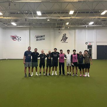 A group of ten men standing on an indoor soccer field, posing for a photo.