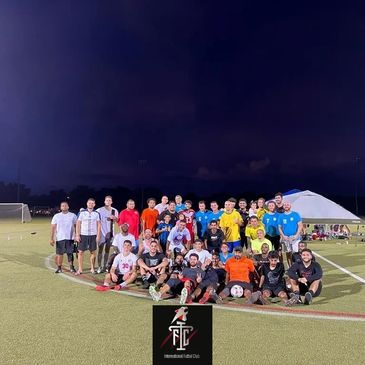 Large group of soccer players posing on a field at night.