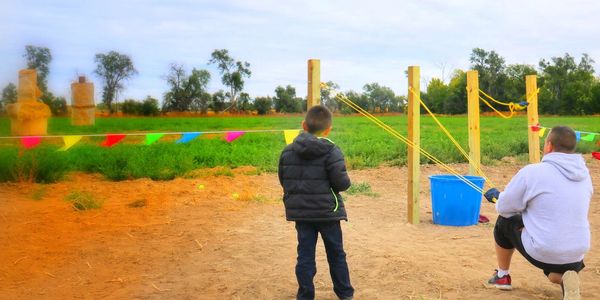 A father and son try their luck at hitting the target with the sling shots.