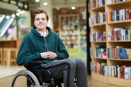 A student in a wheelchair in the library smiling at the camera.
