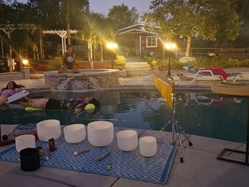 People relaxing near a pool with white bowls on a rug.