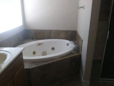 Corner bathtub with dark tile surround in bathroom.