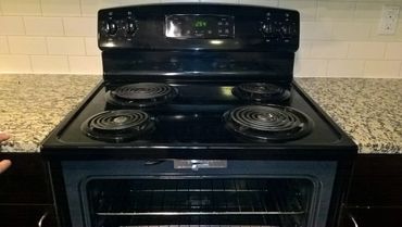 Black electric stove with coil burners and granite countertops.