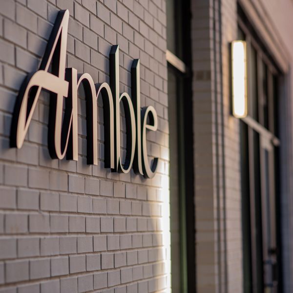 Sign reading 'Amble' on a brick wall.