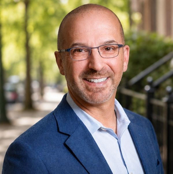 Smiling bald man with glasses in a blue blazer.