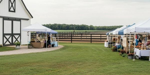 A photo of the farm with a white barn to the left and vendor tents on both sides for possible events