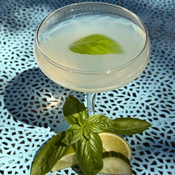 Cocktail with basil leaf garnish on decorative table.