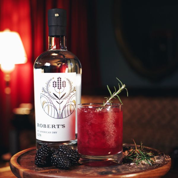 Bottle of Roberts gin and a red cocktail with blackberries and rosemary.