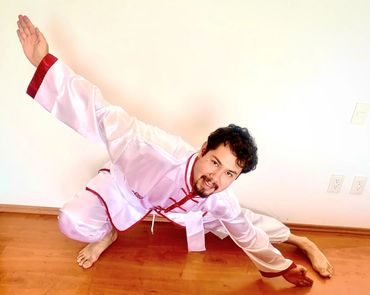 Man in white martial arts uniform performing a dynamic pose indoors.