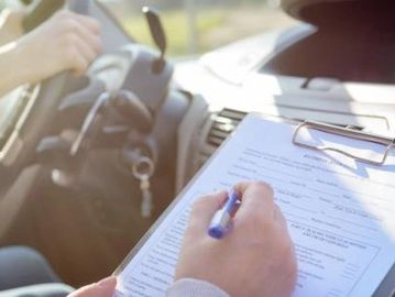 Person filling out a form inside a car with the driver holding the steering wheel.