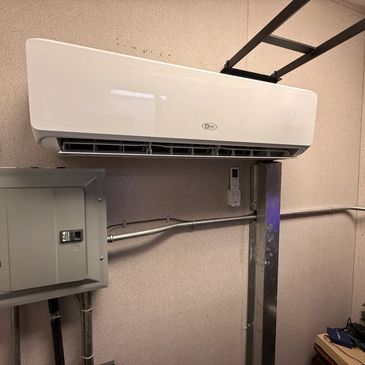 Wall-mounted white air conditioning unit in a utility room.