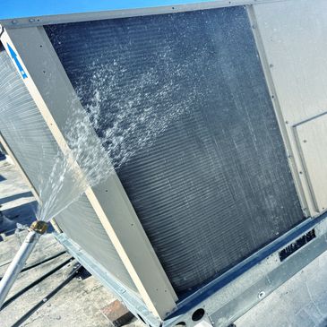 Cleaning an air conditioning unit's condenser coil with water spray.