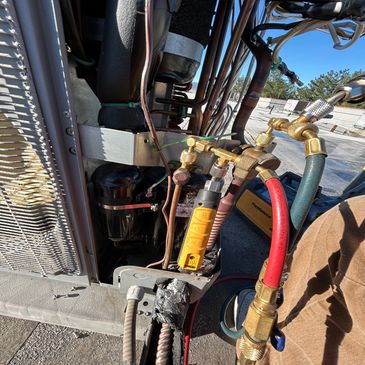 Technician working on HVAC system with manifold gauge and hoses.