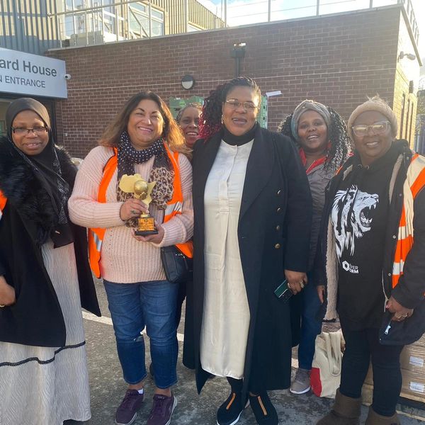 Group of women smiling outside Maynard House, one holding a trophy.