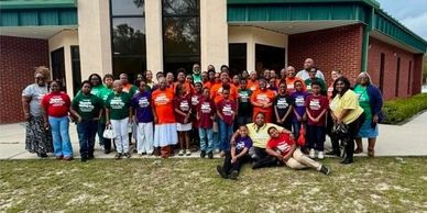 Group photo of diverse people wearing colorful shirts outside a building.