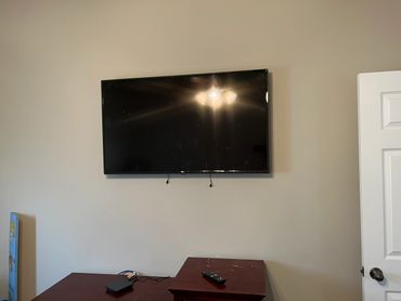 Wall-mounted TV above a wooden table with remote and device.