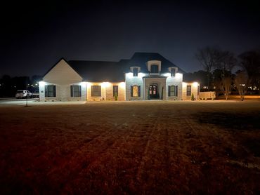 Illuminated large house at night with a spacious lawn.