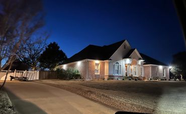 Well-lit suburban house with a large driveway at dusk.
