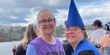 Two smiling women by a lake, one wearing a blue wizard hat.