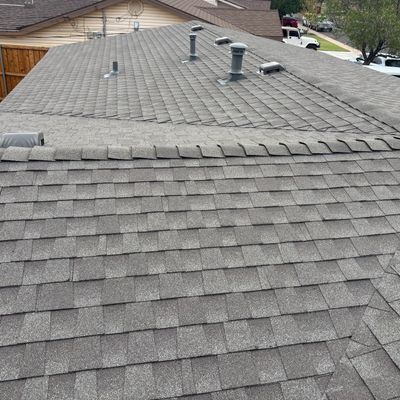 View of a gray shingled roof with multiple vents and pipes.