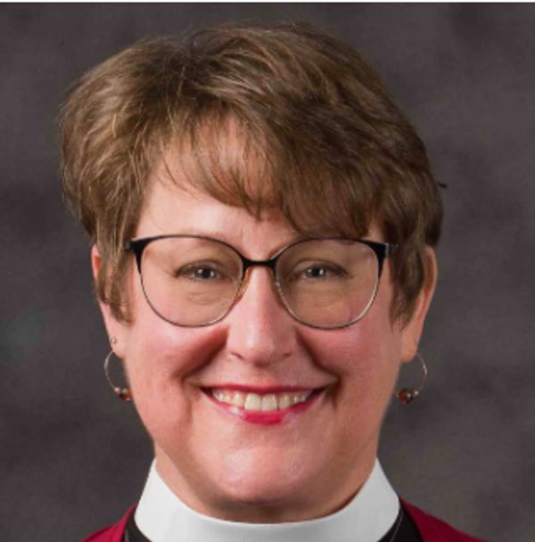 Smiling woman with glasses and short hair against a gray backdrop.