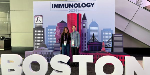 Two women standing in front of an Immunology 2026 Boston backdrop.