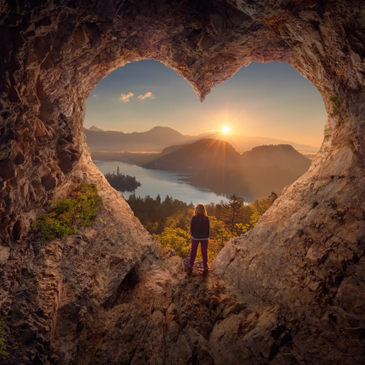 Une femme debout dans un coeur de roche fessant face à des montagnes ensoleillées.