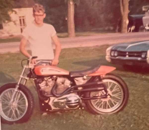 Young man standing with a vintage motorcycle on grass.