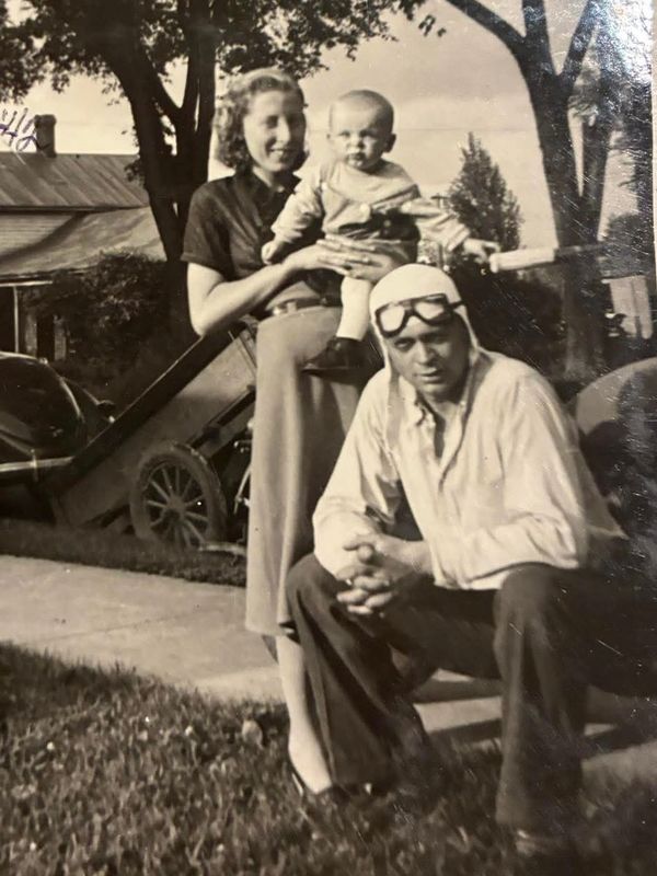 Vintage family photo with mother holding baby and father in aviator goggles.