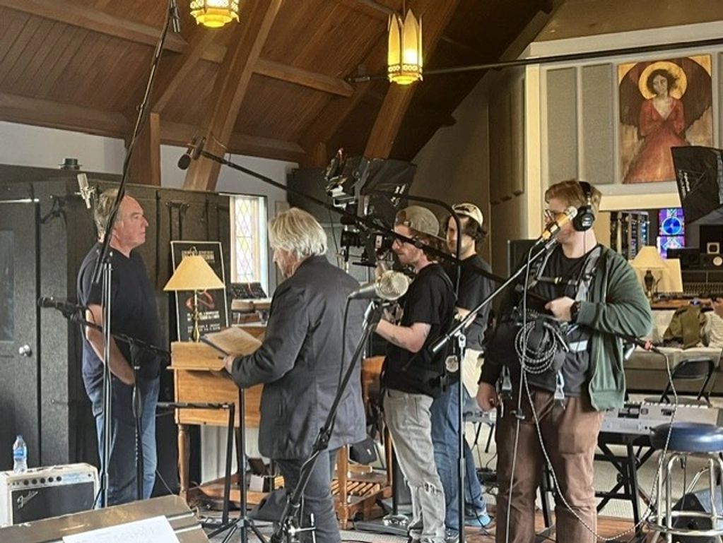 A group filming inside a wood-paneled room with religious artwork.