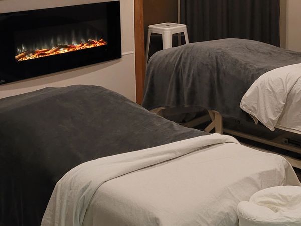 Cozy couple's massage room with two tables, warm fireplace, private shower and calming decor.