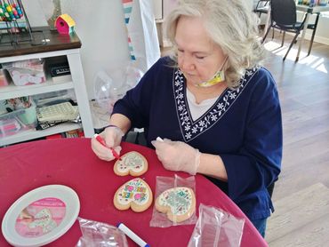 Woman decorating heart-shaped cookies with colorful markers at a table.