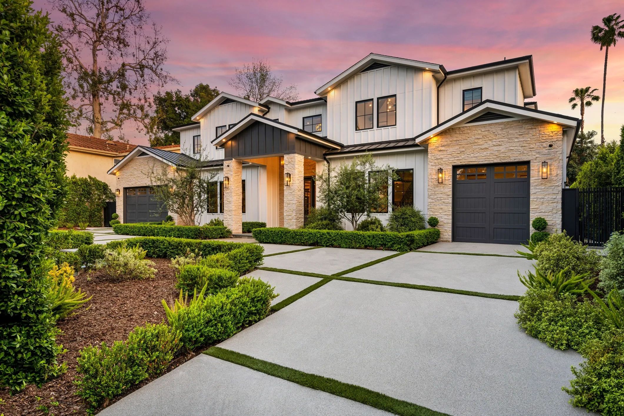 Modern two-story house with stone accents and lush landscaping at sunset.