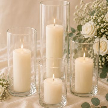 Four lit white candles in glass holders with flowers.