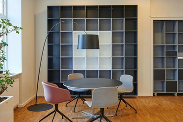 Modern office meeting area with round table, four chairs, and large shelving units.