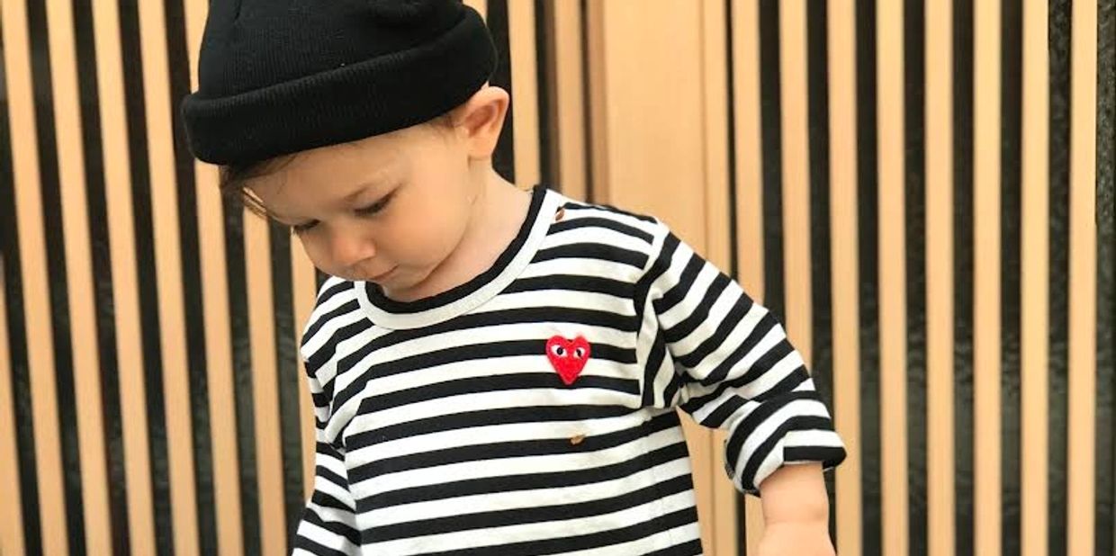 A toddler in a black beanie and striped shirt looks down thoughtfully.